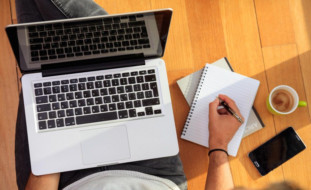 person taking notes beside laptop